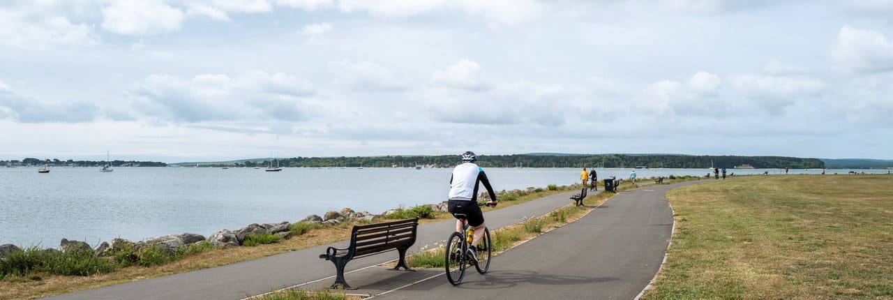 Whitecliff Park Poole with cyclists on the cycle path overlooking Parkstone Bay and Harbourside Park towards Poole Quay